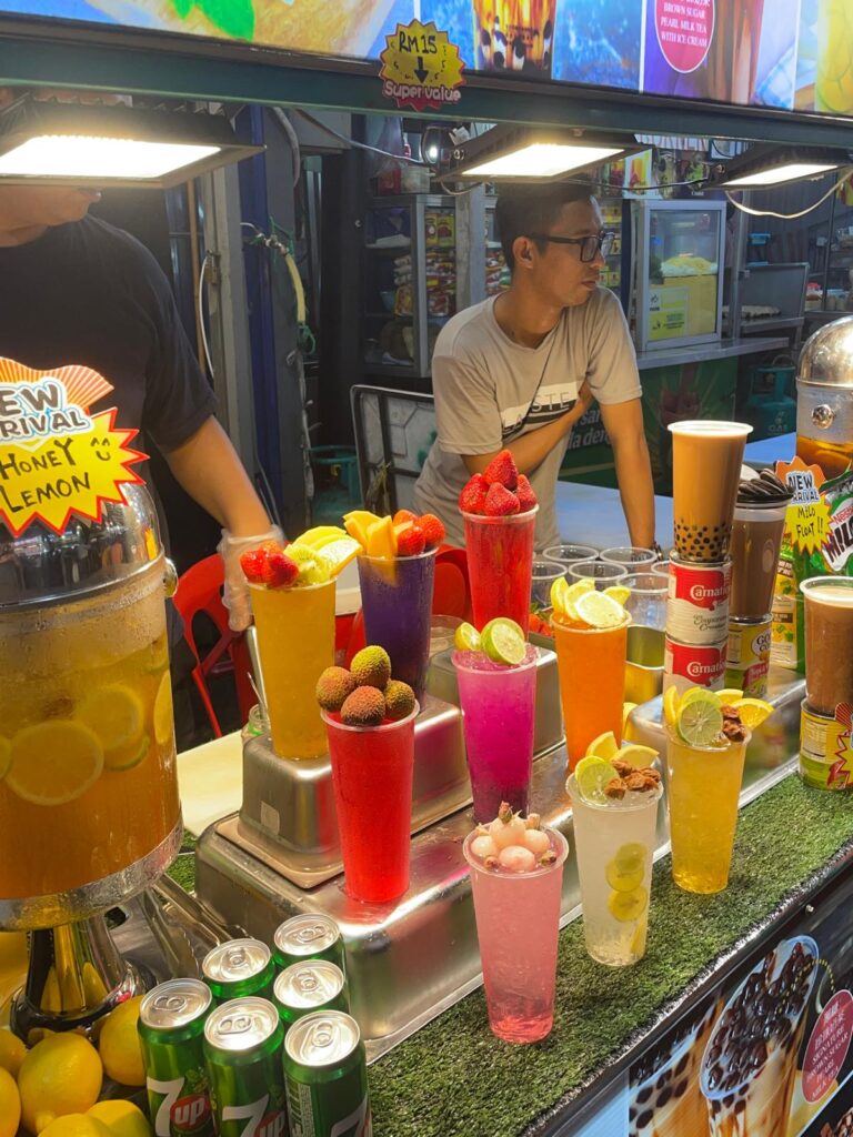 A drink stall at a Malaysian street market selling several brightly-coloured drinks with sliced fruit at the top