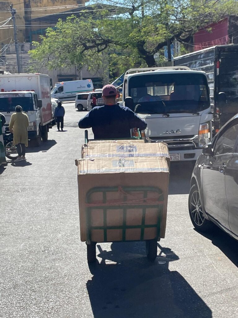 A man pulling a trailer full of boxes along a busy road in Asuncion, Paraguay, he is surrounded by vehicles