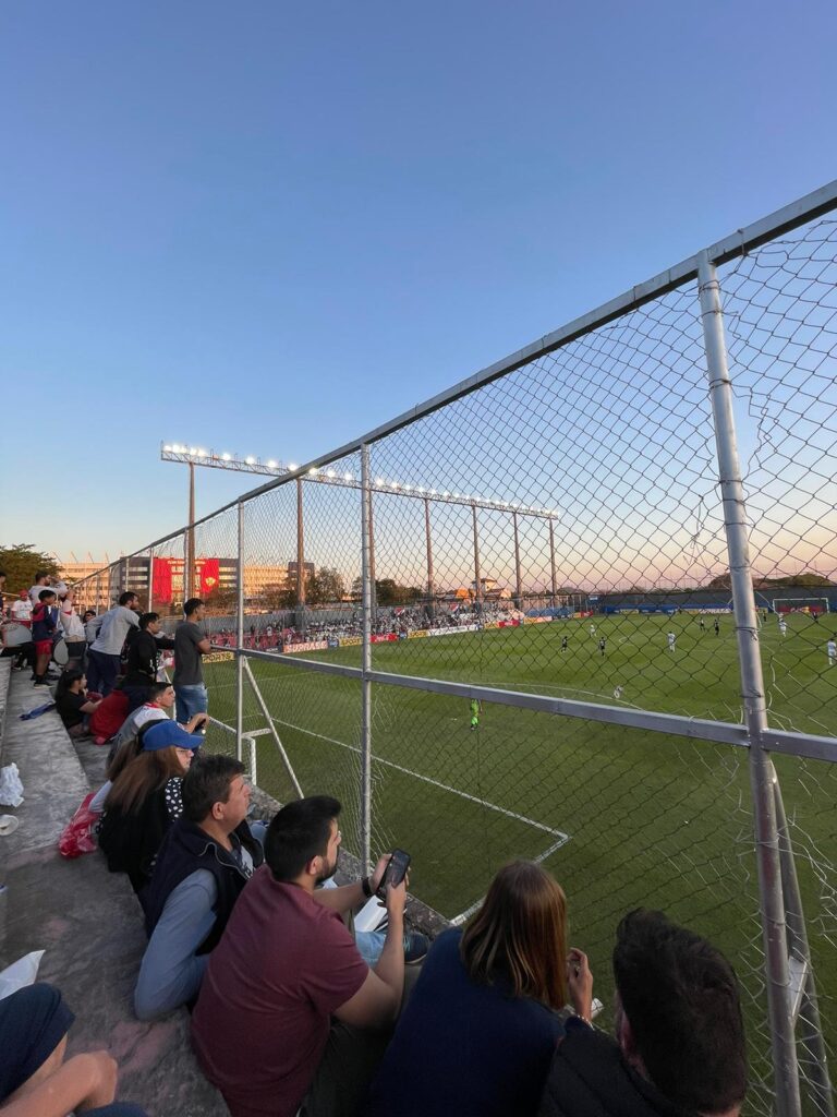 A series of football fans watch Libertad play from behind a fence in Asuncion, Paraguay