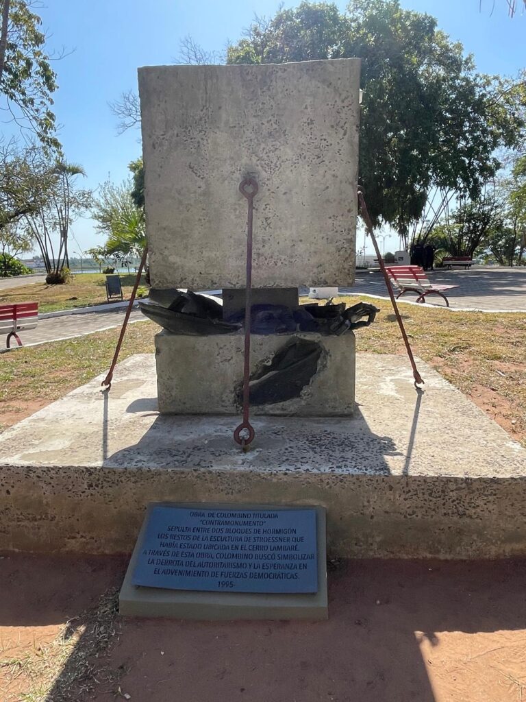 A statue of Paraguayan dictator Alfredo Stroessner being crashed under a large rock