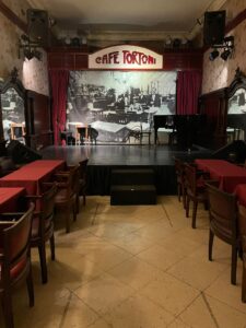 A stage with red curtains and black-and-white photos surrounding it, with a sign that says Cafe Tortoni just above it