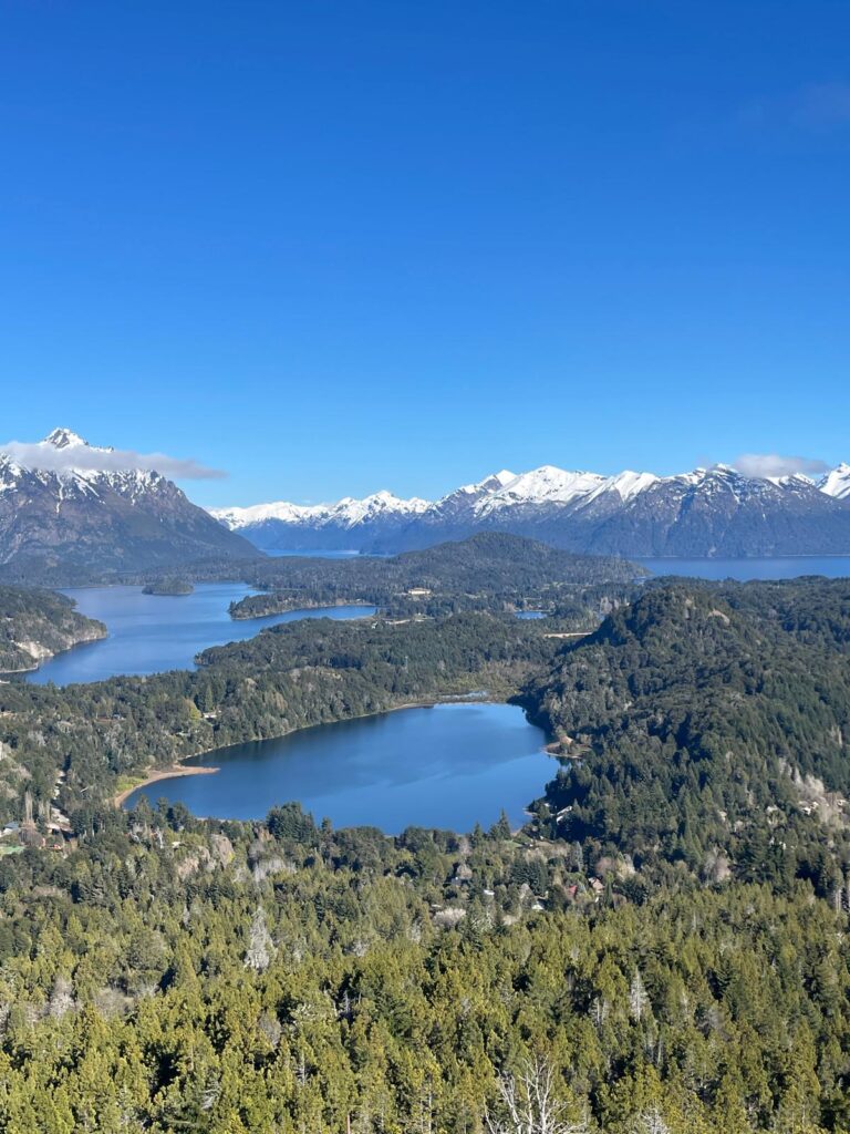 The bright blue lakes, green pine forests and snow-capped mountains  visible from the top of Cerro Campanario in Bariloche