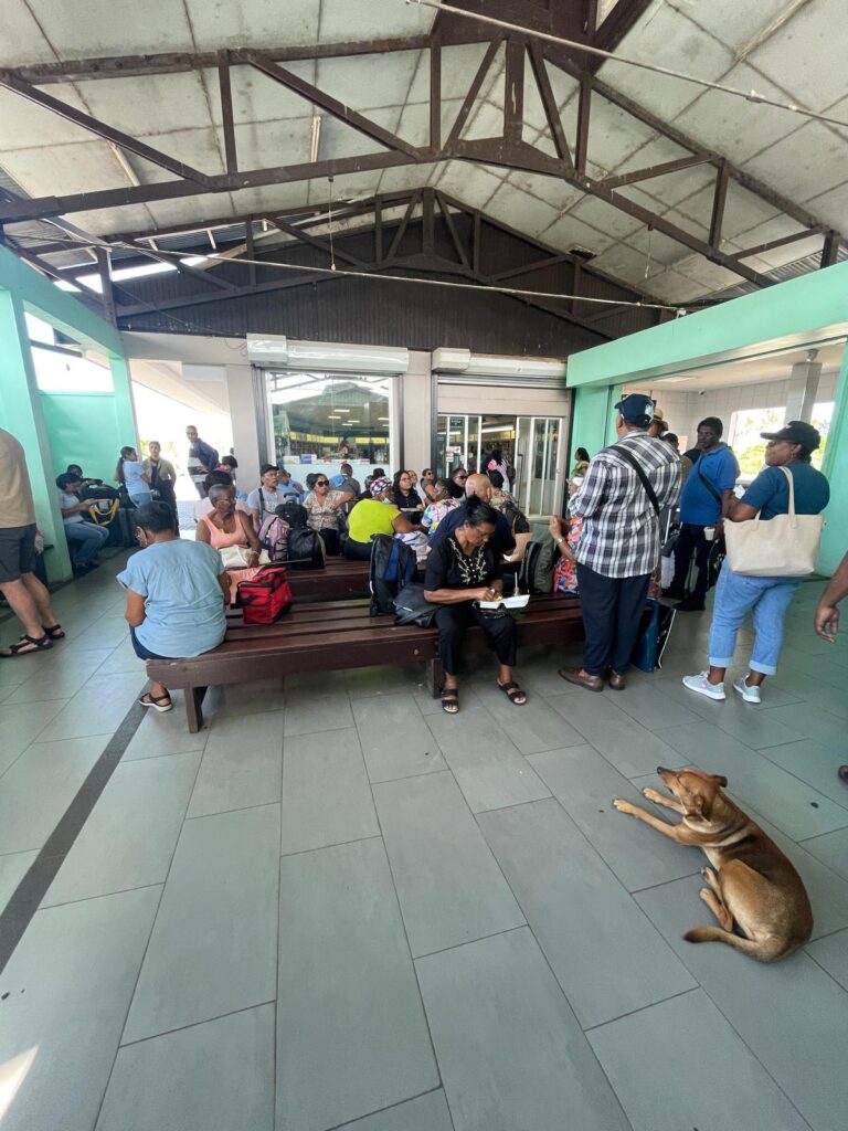 A large group of people waiting for the ferry between Guyana and Suriname. A stray dog sits beside them