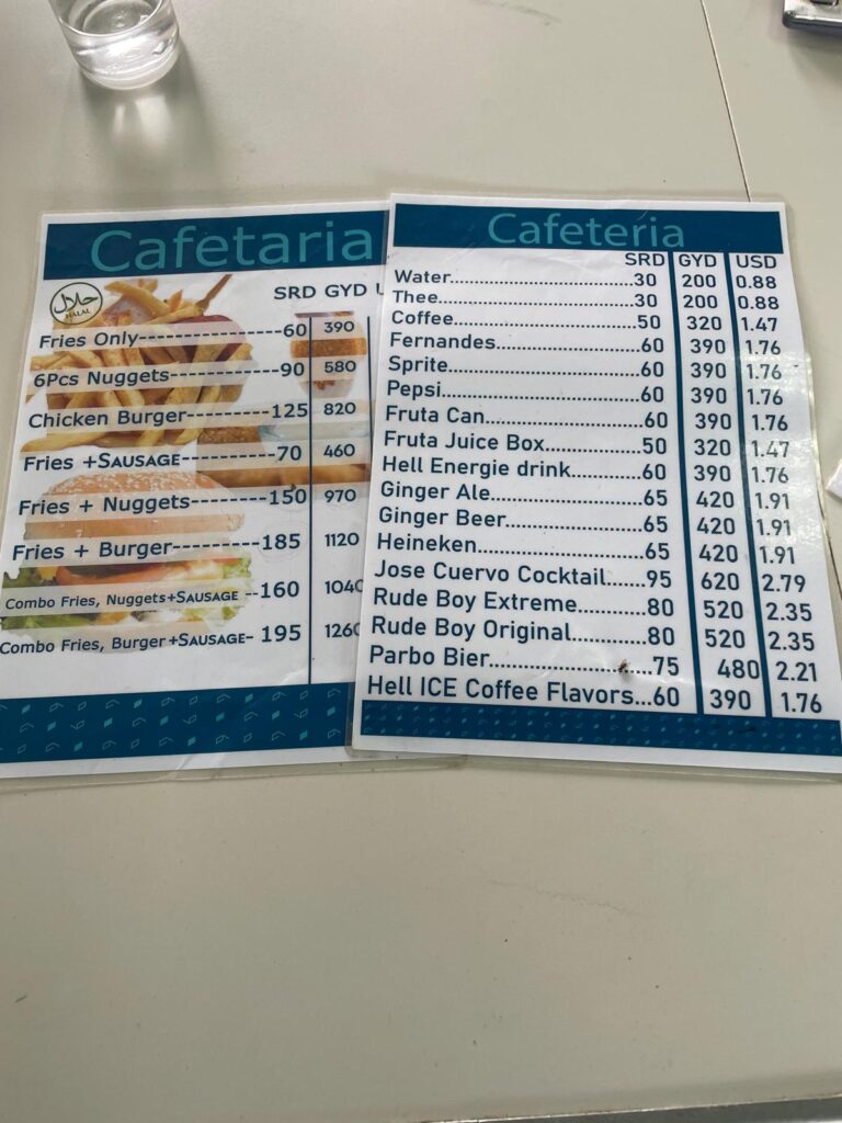 Menus at the canteen on Suriname's side of the Suriname/Guyana border at South Drain. They show a series of items ranging from water, coffee and coke to fries, chicken nuggets and burgers. Prices range from US$0.88 for a water or tea (spelt incorrectly as "thee") to US$5.72 for a combo of fries, a burger and a sausage