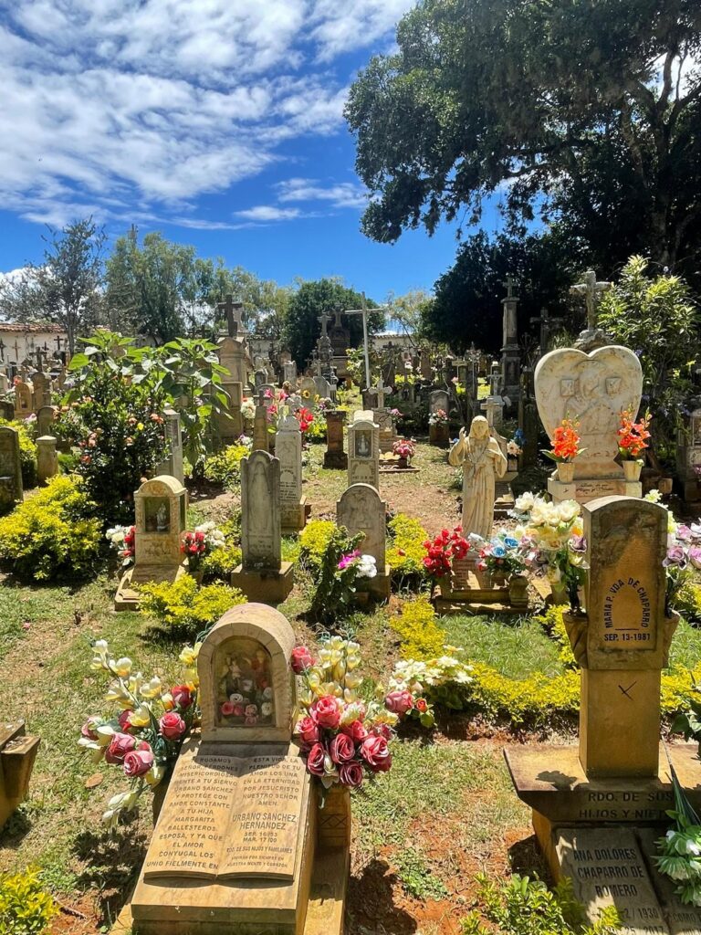 A colourful graveyard in Barichara, Colombia. There are several flowers around the stone graves in all sorts of colours. The blue skies in the background add to the scenic views.