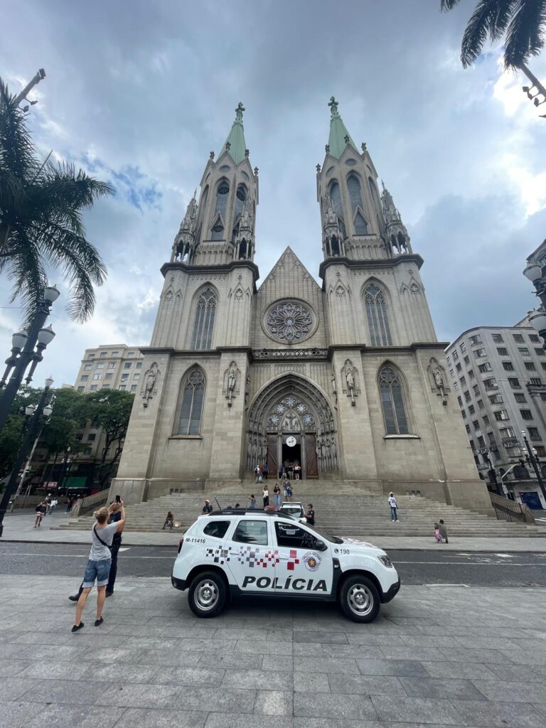 The Metropolitan Cathedral of Sao Paulo, with a police car in front of it and a tourist taking photos