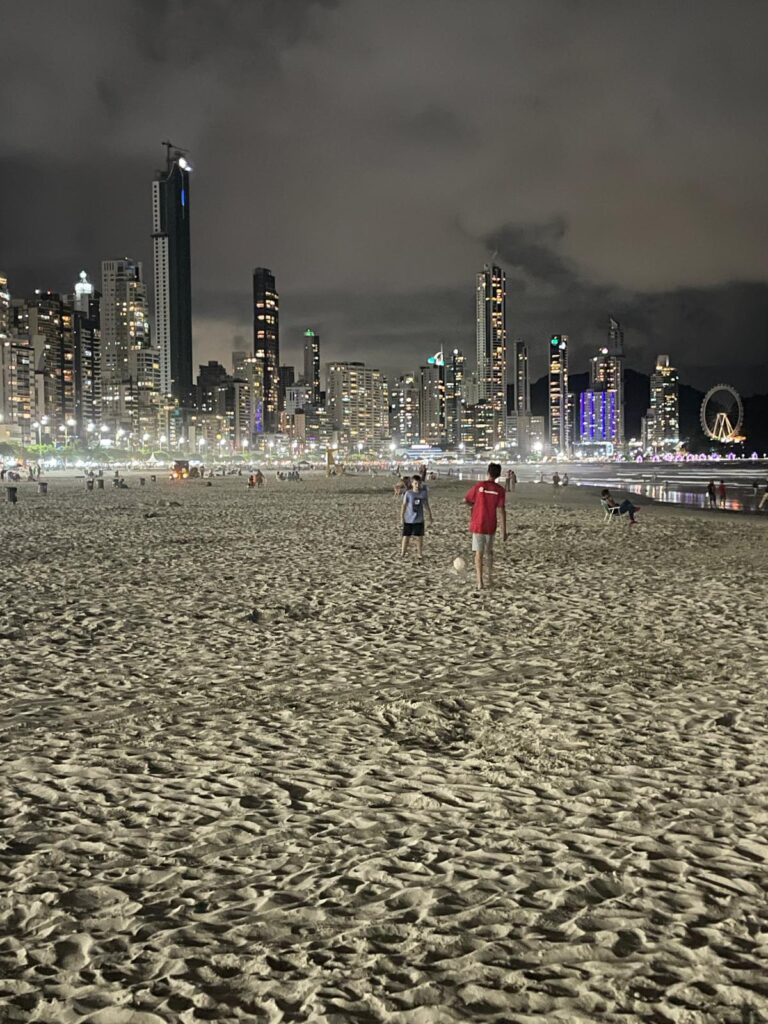 Bright skyscrapers in the background lighting up the night's sky as people play football on the beach in Camboriu, Brazil