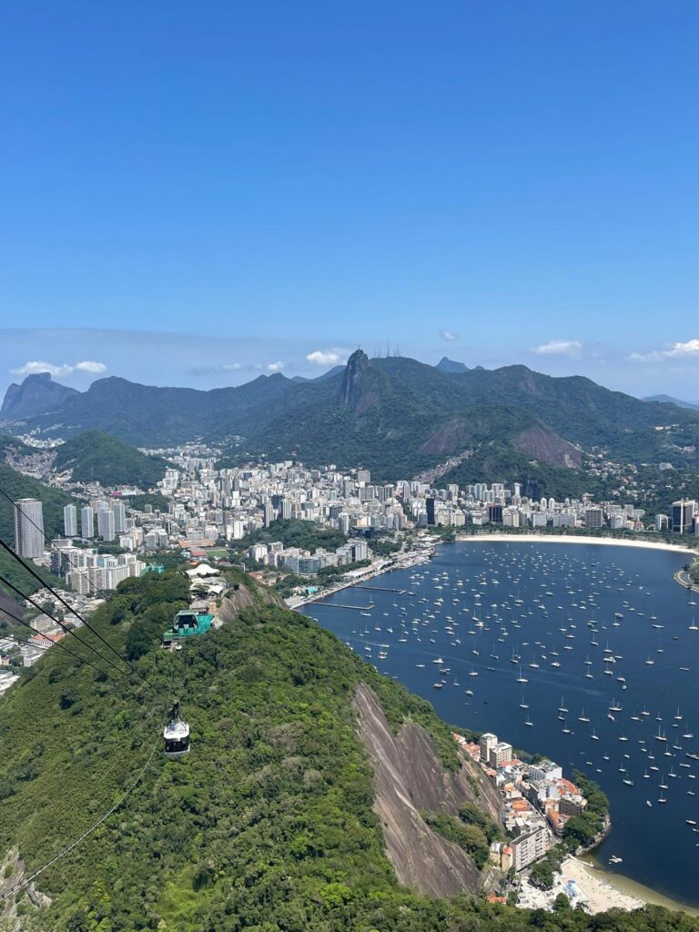 Views of Rio de Janeiro from the top of Sugarloaf Mountain. You can see the bay surrounding Botofogo Beach as well as many tall buildings in the distance.